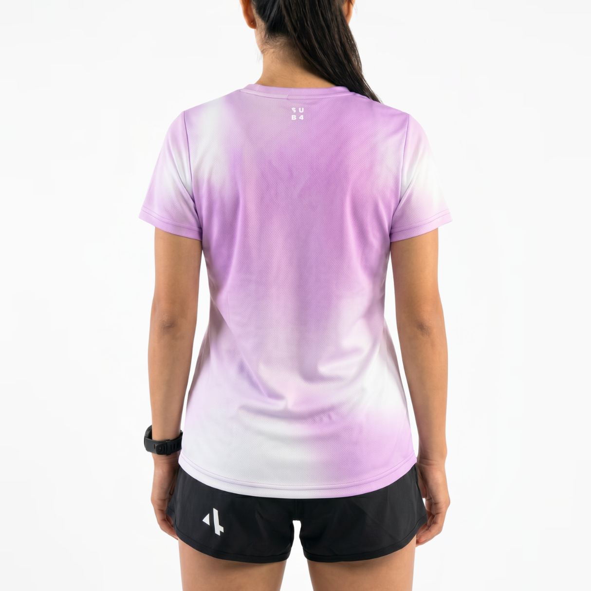 Back view of woman wearing a lilac gradient running t-shirt and black running shorts on a white background.