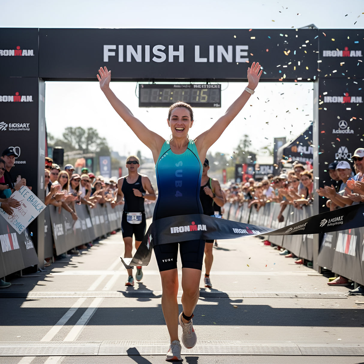 Athlete crossing the finish line of an Ironman triathlon with confetti falling.