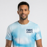 A man wearing a light blue and white tie-dye t-shirt with 'CHRIS MELBOURNE 26' printed in black on the chest, set against a plain light gray background.