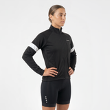 Side view of woman wearing a black cycling thermal jacket and black cycling shorts with white reflective accents on a light gray background