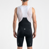 Back view of man wearing black cycling bibs with white straps and a mesh cycling base layer under shirt.