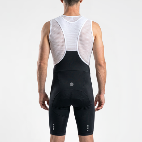 Back view of man wearing black cycling bibs with white straps and a mesh cycling base layer under shirt.
