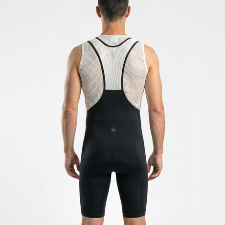 Back view of man wearing a classic black and white cycling bib with a white mesh cycling base layer on a light gray background