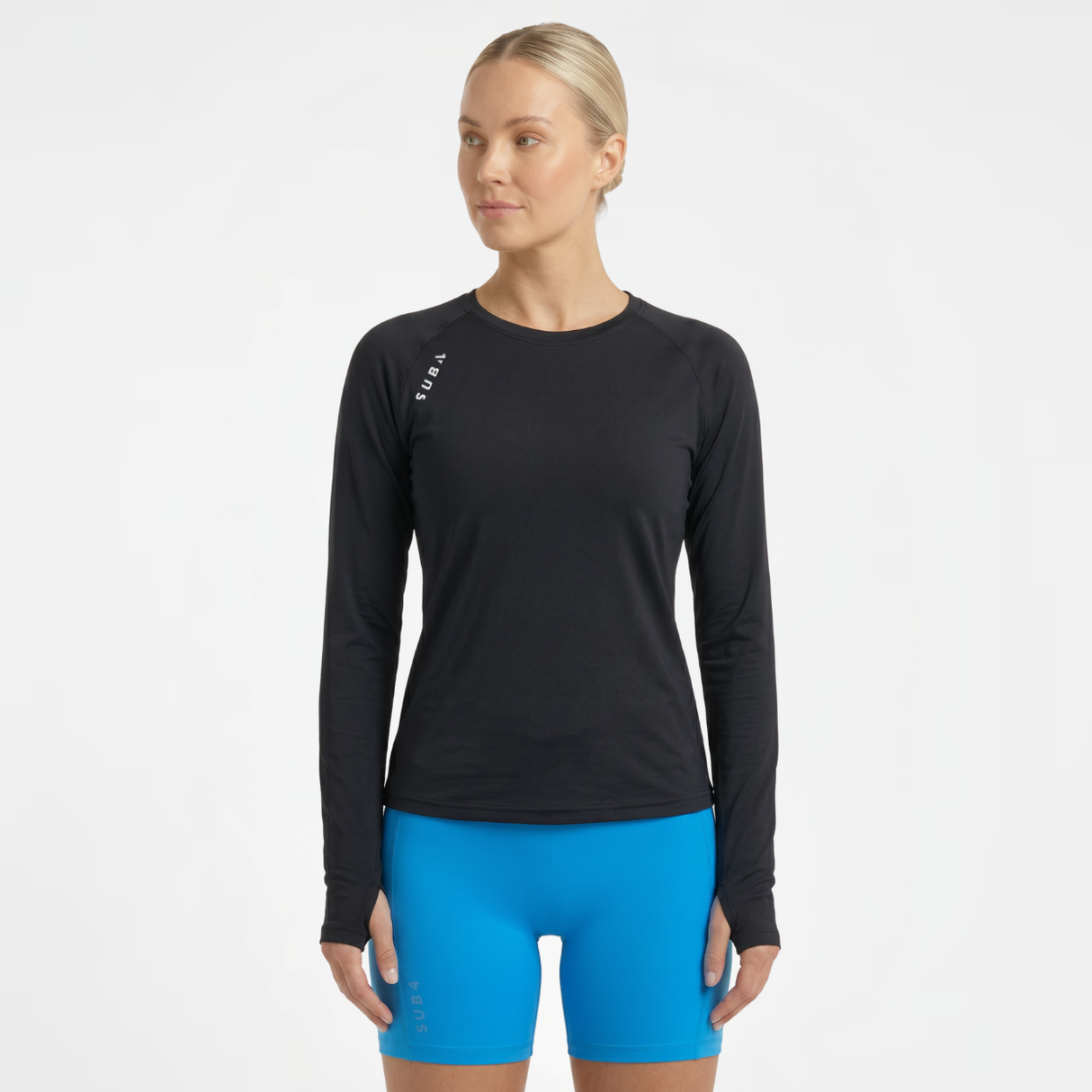 Woman wearing a black long-sleeve running fitness top and blue shorts on a white background