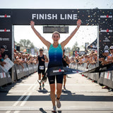 Athlete crossing the finish line of an Ironman triathlon with confetti falling.